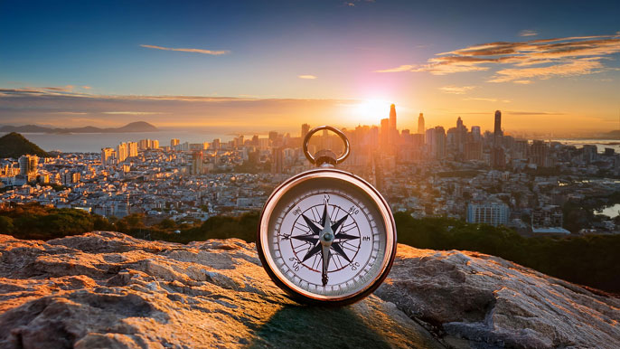 A glowing compass placed on a rocky path with a vibrant city skyline in the background, symbolizing vision and direction leading to entrepreneurial success.